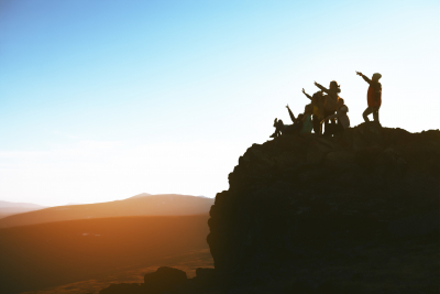 group of people in a top of the big rock raising arms